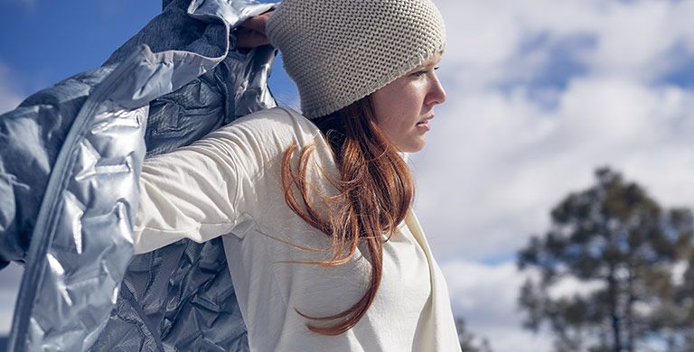 A woman putting on an insulated jacket.