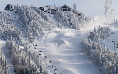 Two chair lifts snake up a snow-covered mountain. At the top is a ski lodge.  