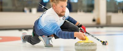 A man with perfect form begins to slide the curling stone across the ice. 