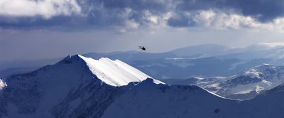  A helicopter hovers above a pristine snowfield in the mountains, preparing to drop off skiers.