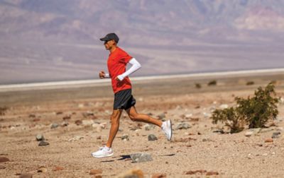 A man, dressed in sun-protective running gear and white running shoes, stretches his stride on a desert run.