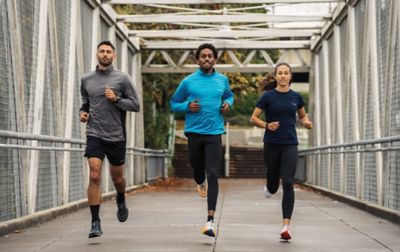 Three people, wearing Columbia Sportswear running shoes run across a footbridge. 