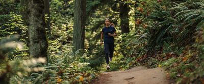 A woman wearing Columbia Sportswear running shoes runs on a forest trail. 