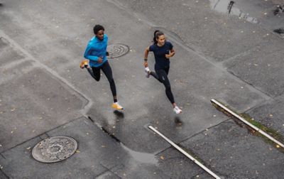 A man and woman run down a rain-soaked street, both maintaining perfect strides.