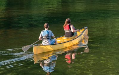  Two women, both wearing life vests, paddle in unison through emerald-colored water.