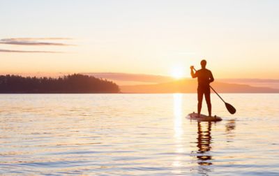 Une personne fait du paddle sur un lac au coucher du soleil.