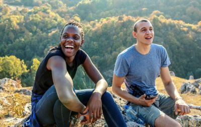 Two people sitting on rocks at the top of a hill smiling.