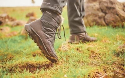 Une personne portant des bottes imperméables Columbia Sportswear marchant dans un champ humide et boueux.
