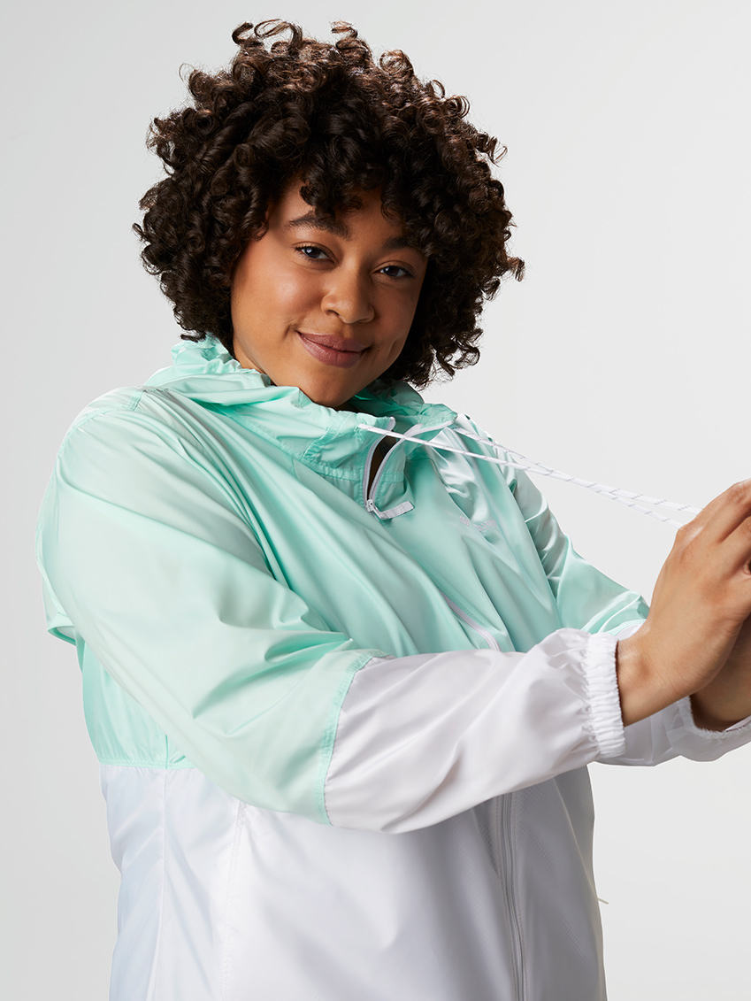 Woman tugging the drawcords of a light blue and white windbreaker.