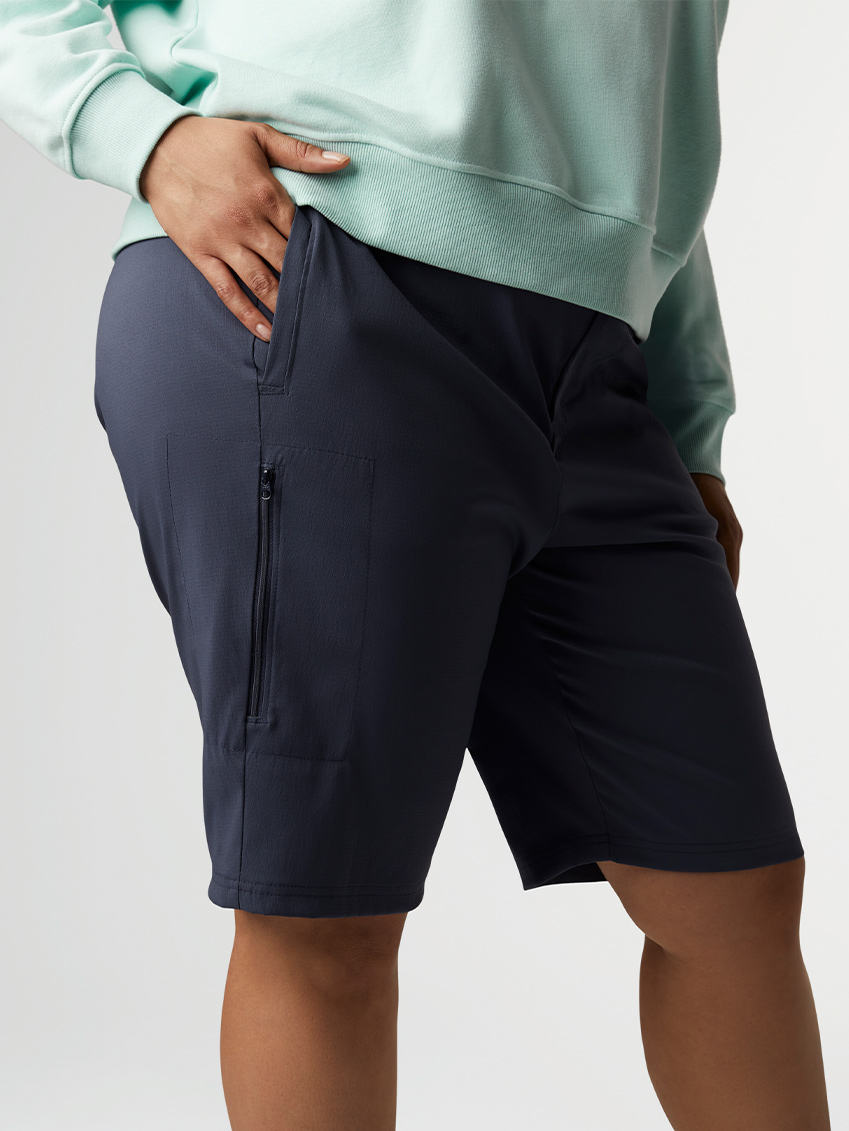 Close-up of a woman putting her hand in the pocket of navy blue hiking shorts.