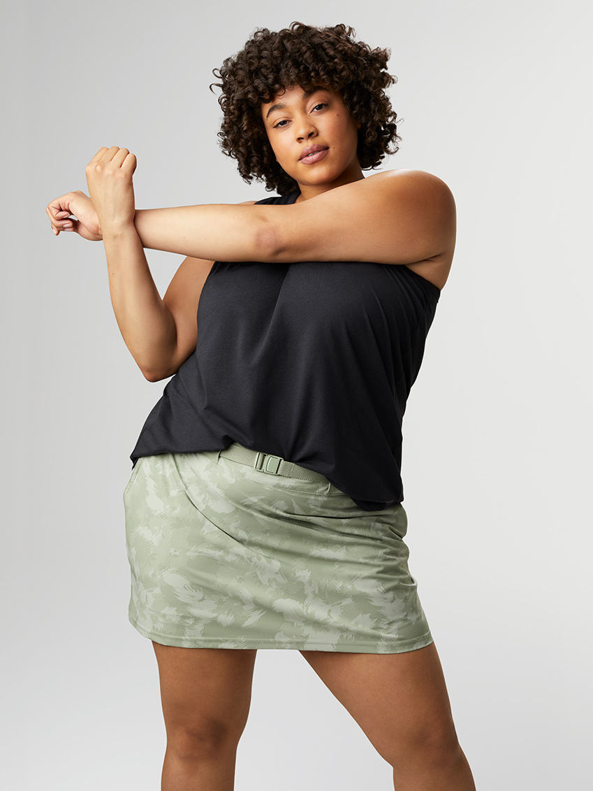 Woman in a black tank and camo skirt stretching her arm.