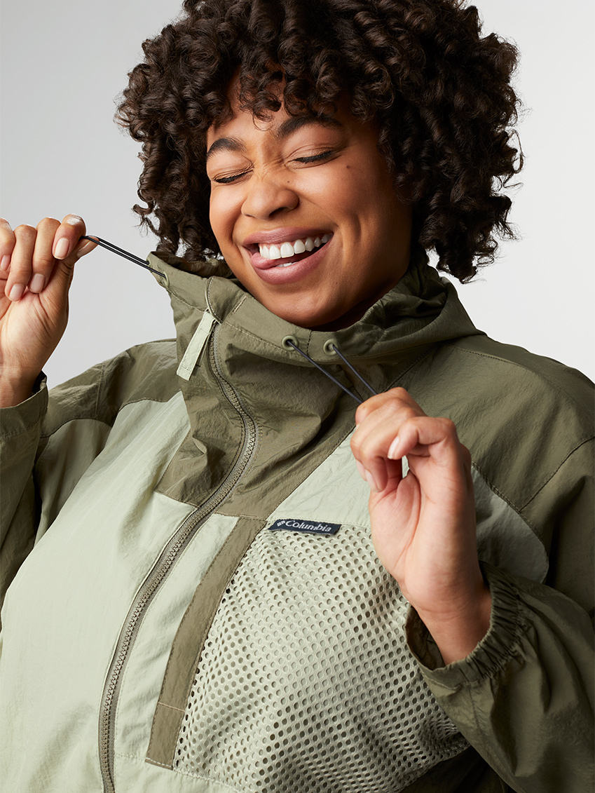 Woman making a goofy face while pulling the drawcords of her green windbreaker jacket.