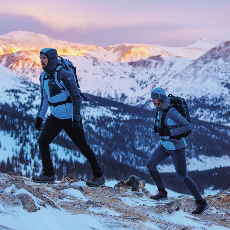 Man and woman hiking a snowy mountainside in Titanium gear. 