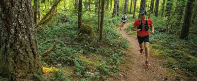 A man in a red Columbia Sportswear shirt runs through a wooded green forest.