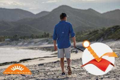 Model walking on a beach in the blue Tamiami button up short sleeve shirt. Omni-Shade logo is on the bottom left and a graphic showing how the sun's rays are blocked by fabric is on the bottom right.