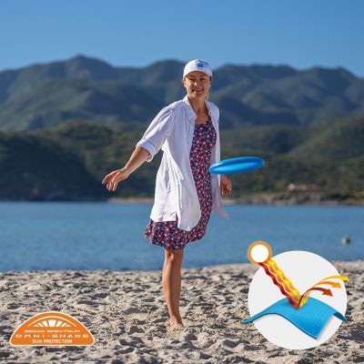 A woman playing frisbee on a beach with a button-up and printed Freezer III Dress. Omni-Shade logo is on the bottom left and a graphic showing how the sun's rays are blocked by fabric is on the bottom right.