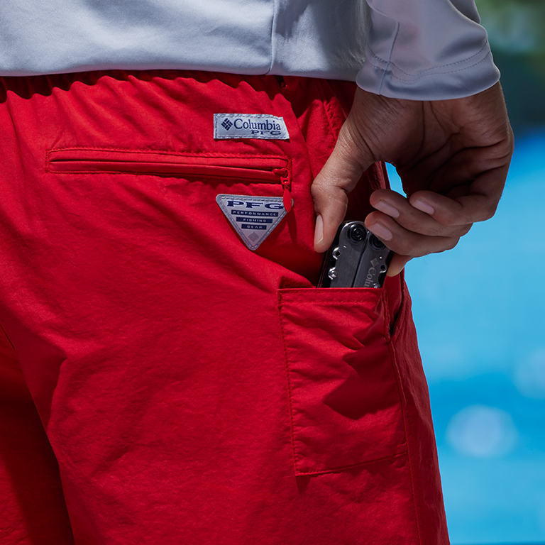 Close up of back right pockets: one is the zippered security pocket and the other is the drop-in pocket with the model dropping in a multi-tool pocket knife.