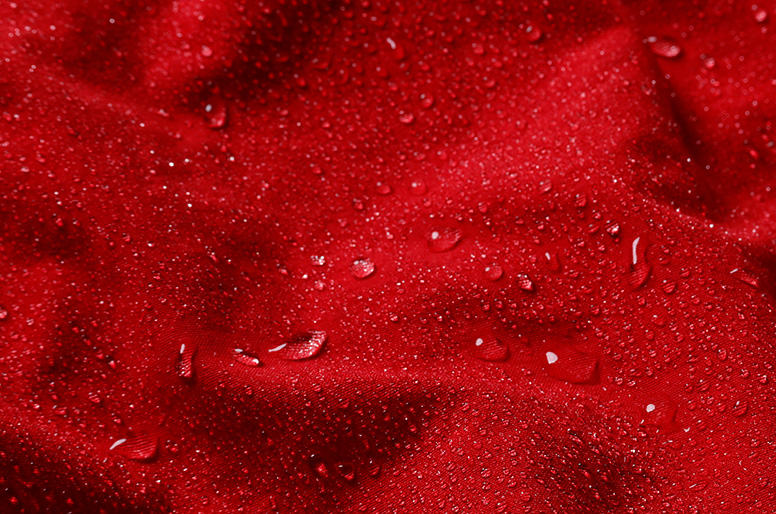 Macro shot of the bright red shorts fabric showing how water beads up on the surface because of the quick-dry treatment.