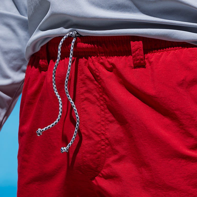 Close up of drawstring integrated into the elastic waistband of the bright red water shorts.