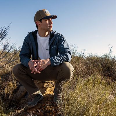 A model squatting down in the khaki cotton-blend pants on a high desert trail to show that they have stretch.
