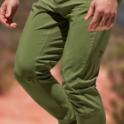Model in mid-stride to show the stretchy fabric of the green pants.