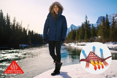 A woman walks along a snowy river, staying warm in a thermal-reflective jacket.