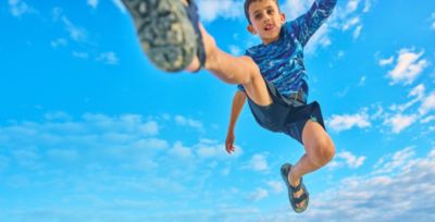 A cute kid jumping into the air in sun blocking gear.
