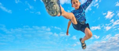 A cute kid jumping into the air in sun blocking gear.