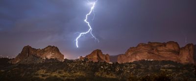 A jagged bolt of lightning illuminates the night sky as its claw-like tentacles reach down to a series of rocky outcrops.