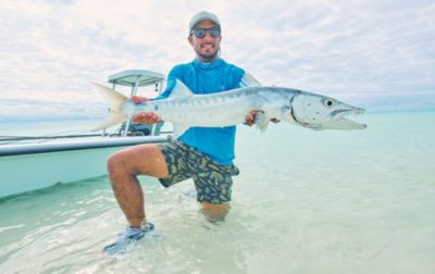 A man wearing PFG fishing apparel displays a large fish before releasing it back into the water.