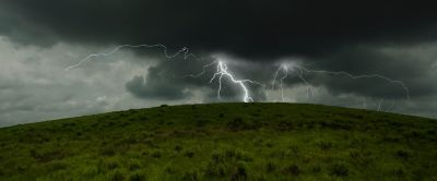 Dark, menacing sky. A lightning bolt with spider-like tentacles strikes the top of grassy, shrub-covered hilltop.