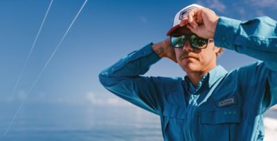 A man on a boat fixing his hat.