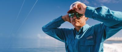 A man on a boat fixing his hat.