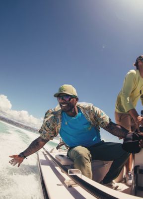 An angler soaking in the sun and touching the water while on a speeding boat.