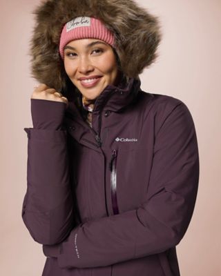 A model wearing a light purple long-sleeve shirt, matching beanie, a long puffer vest, comfy leggings, and winter boots.