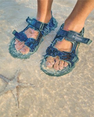 A close-up of kids' sandaled feet in the ocean.