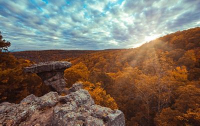 A prominent flat-topped outcrop rises above a hardwood forest with orange foliage.