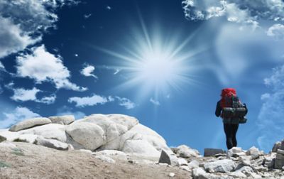 A hiker with a large red backpack, tent, and sleeping pad strapped underneath walks through a boulder field of white granite.