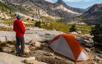 A solo camper has pitched a small tent by an alpine lake.