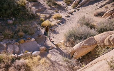 A woman strolls down a sandy trail through a boulder field.
