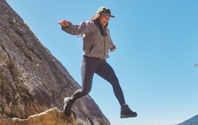 Woman wearing Columbia Hiking leggings jumping off a rock.