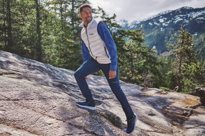 A person hiking over rocky terrain with snow-capped mountains in the background.