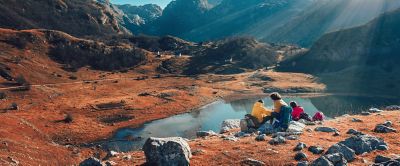 Sunlight streams down as a trio of backpackers relax on rocks above a tranquil alpine lake. 