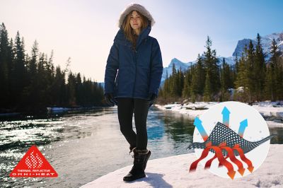 A woman walks along a snowy river, staying warm in a thermal-reflective jacket.