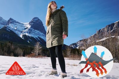 A woman stands in front of a snowy landscape with mountains. She's staying warm in a thermal-reflective jacket.