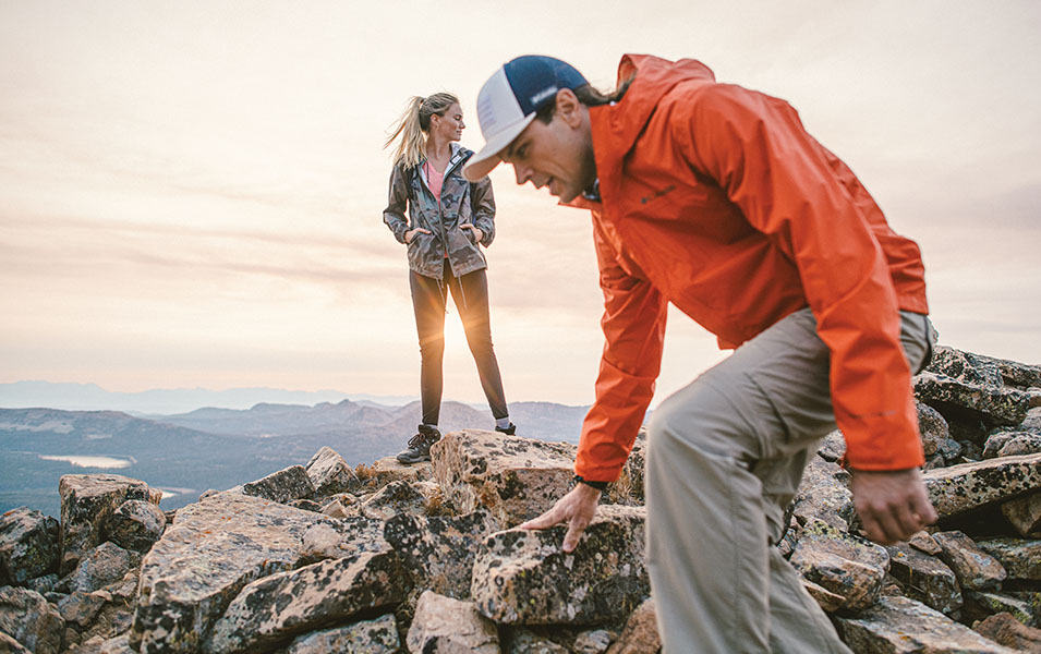 Man and woman walking on the top of mountain at sunset. 