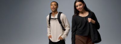 Two students smiling, wearing backpacks and tote bags.