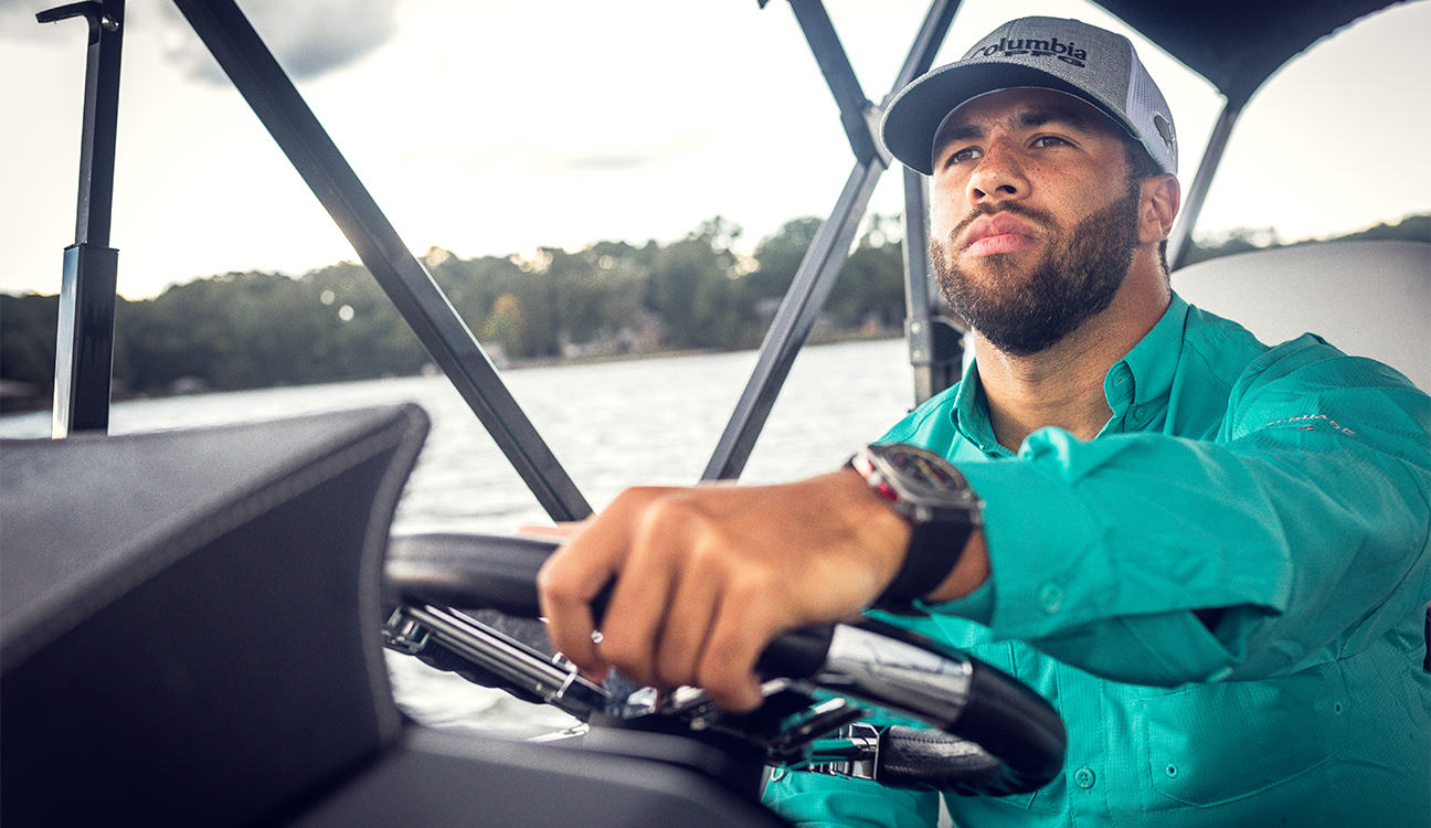 Close-up of Bubba Wallace piloting a boat while wearing Columbia PFG. 