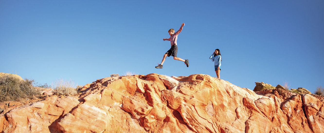 Two kids running along a rocky ridge.