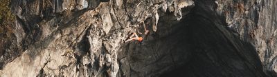 Woman climbing a cave peak above water.